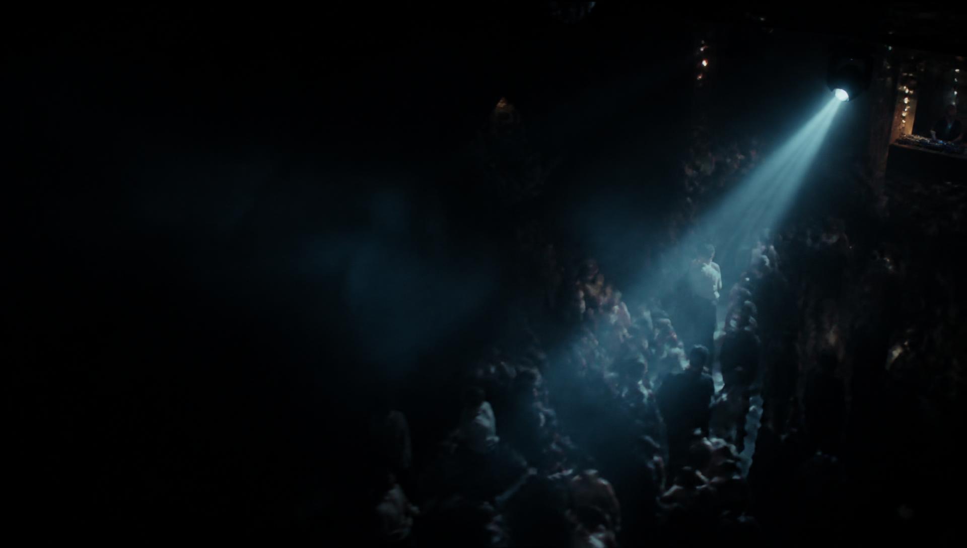Crowd dancing under a single beam of light at a late-night event