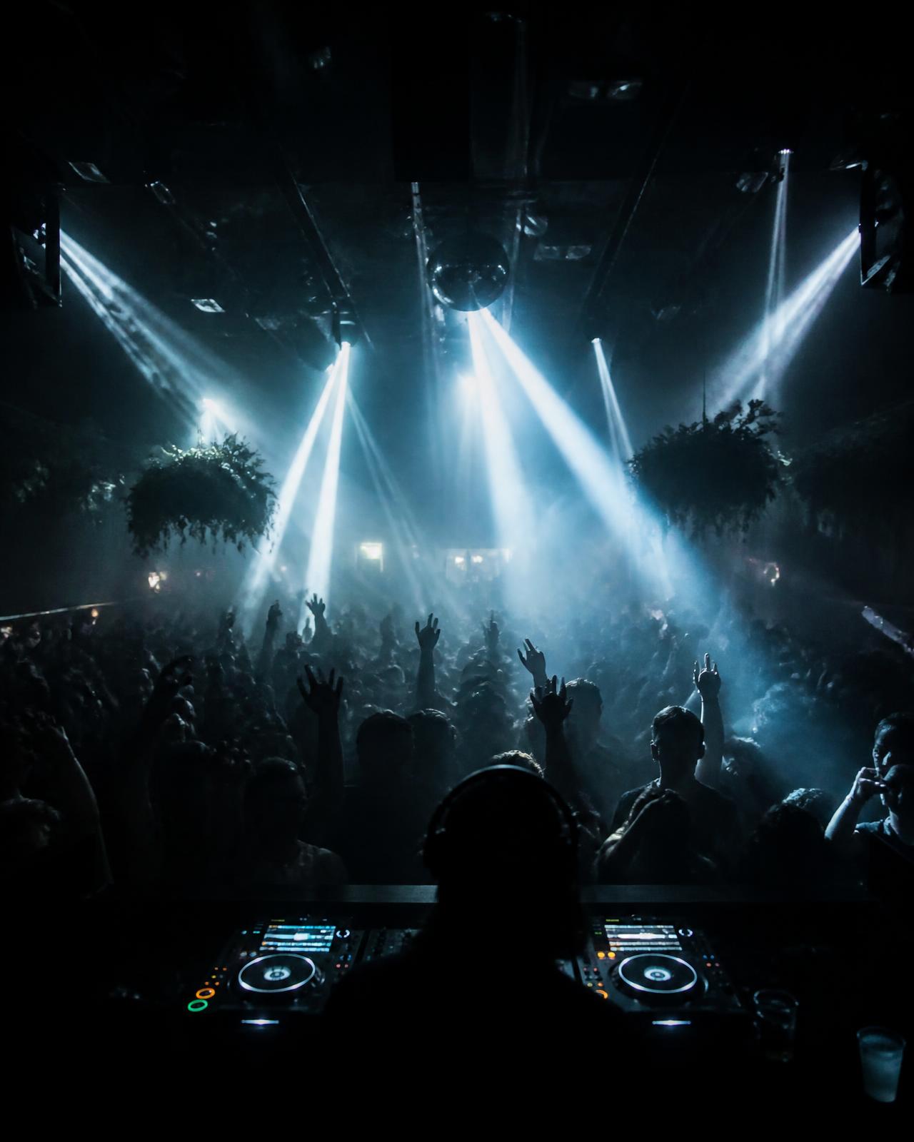 Packed club dance floor seen from the DJ booth with beams of light